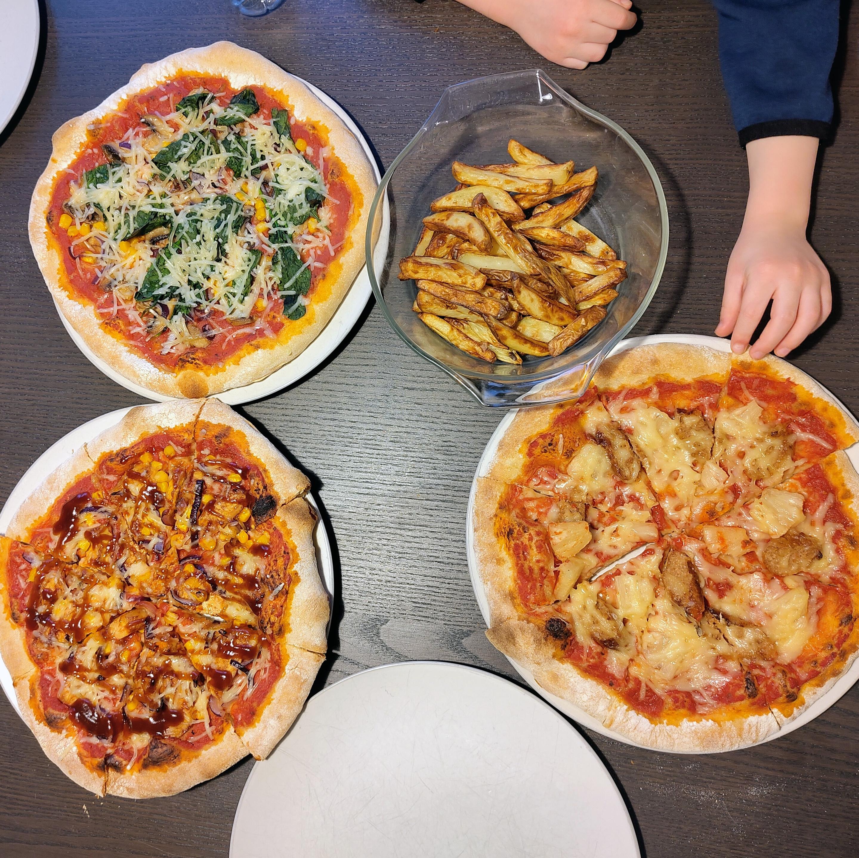 A spread of three homemade vegan pizzas and homemade chips. A child's hand reaches for a slice